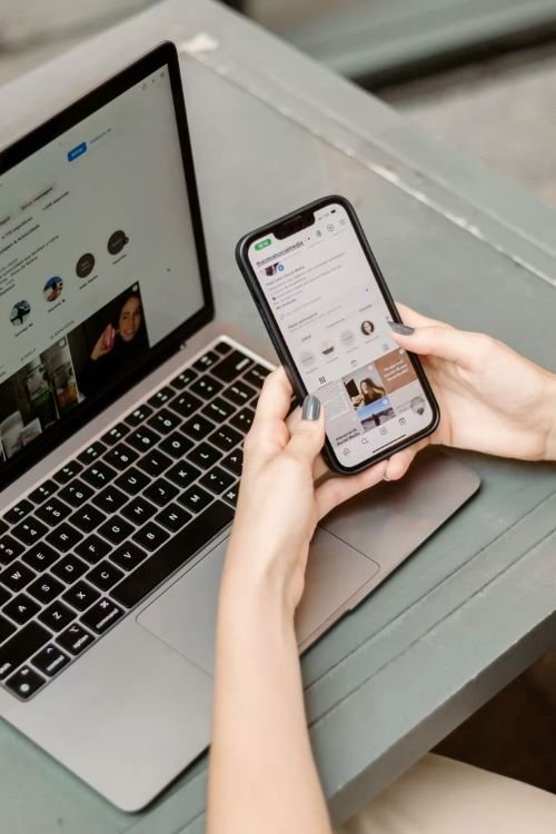 Hands browsing a smartphone next to an open laptop, representing digital strategy and diagnostic consultations for Gleaming