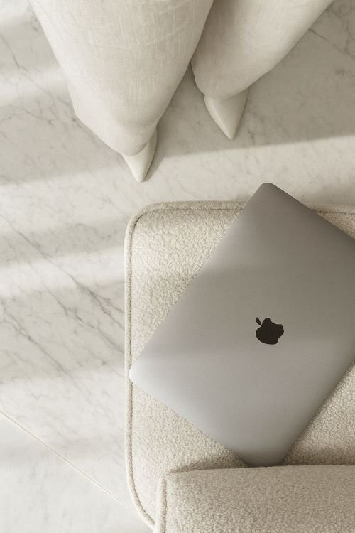 Top-down view of a closed silver laptop resting on a textured bouclé armchair next to marble flooring